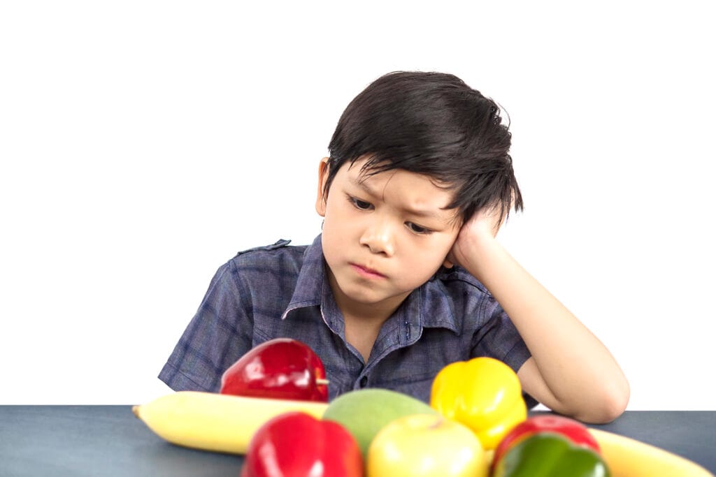 asian boy is showing dislike vegetable expression white background