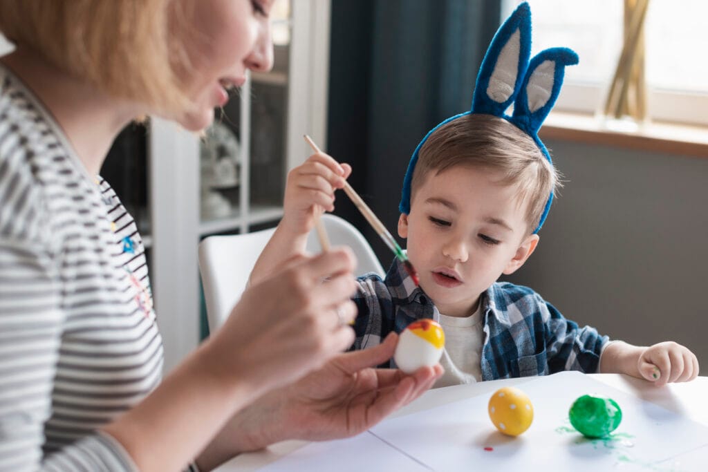 close up mother showing little boy how paint eggs