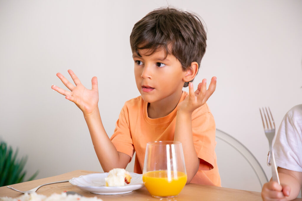 portrait cute little boy eating birthday cake drinking orange juice adorable child sitting table dining room rising hands looking away childhood celebration holiday concept